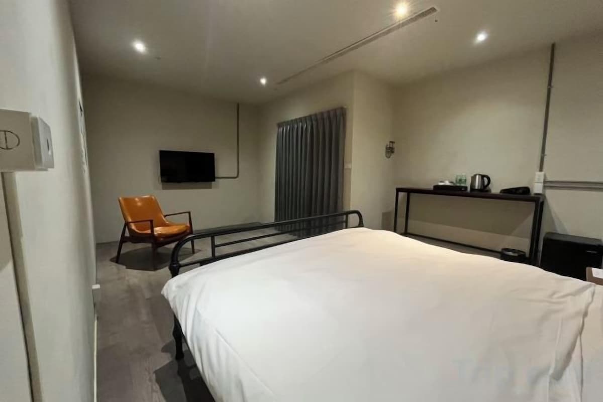 A hotel room with a bed, a chair, a desk, a television, and a window with curtains.