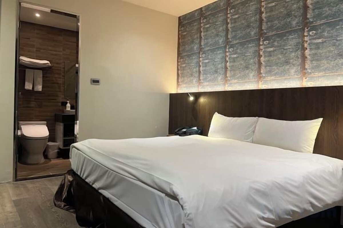 A hotel room with a large bed, a wooden headboard, a nightstand, and a wall-mounted artwork.