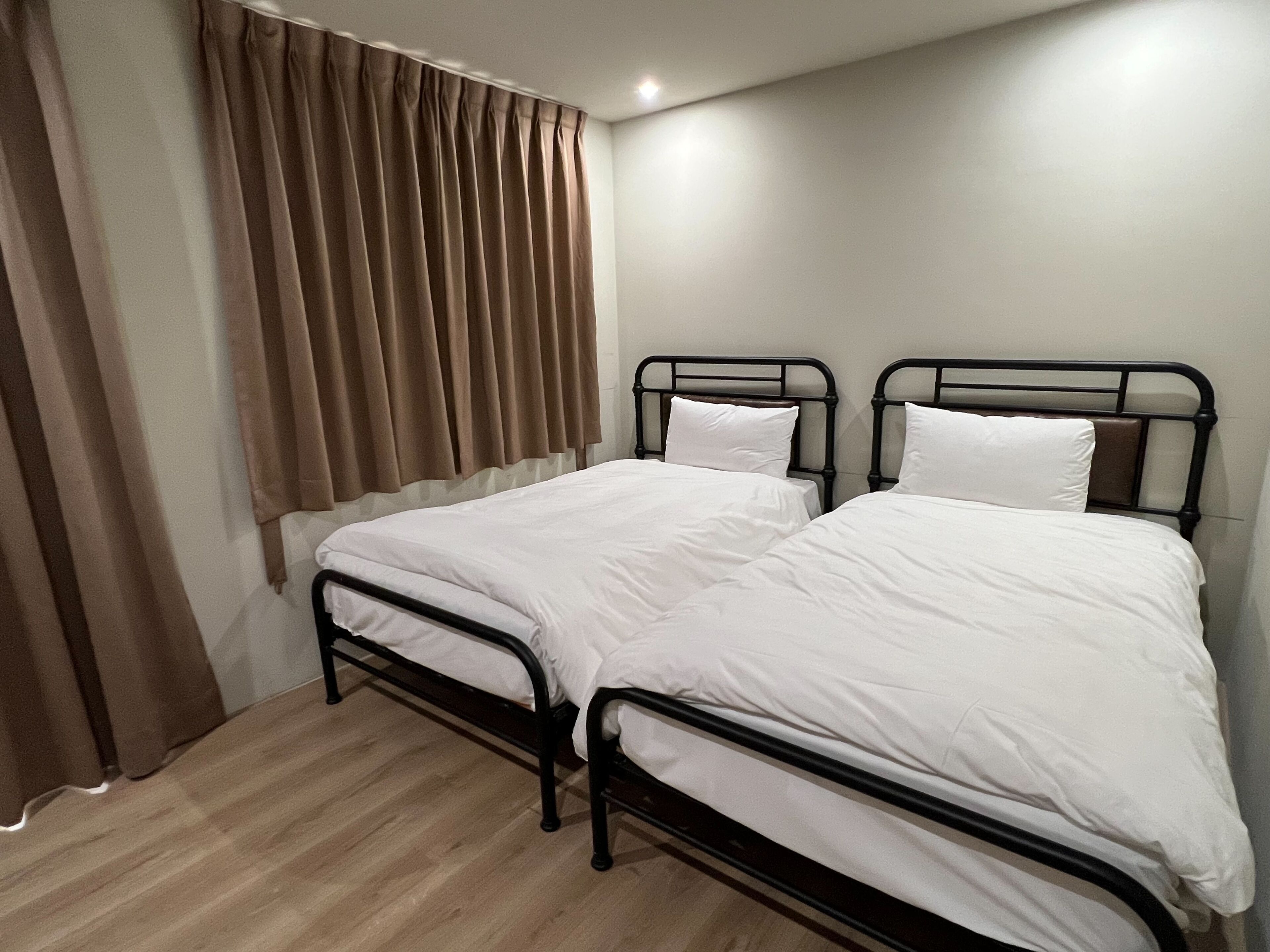Een kamer met twee eenpersoonsbedden, een houten vloer en een raam met bruine gordijnen.