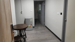 Un couloir étroit qui mène à un coin repas comprenant une table et des chaises, un réfrigérateur et une porte donnant sur une cuisine.