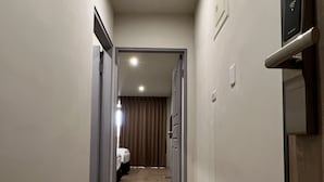 Un couloir étroit au plancher en bois, avec une porte sur le côté droit et un luminaire au plafond.