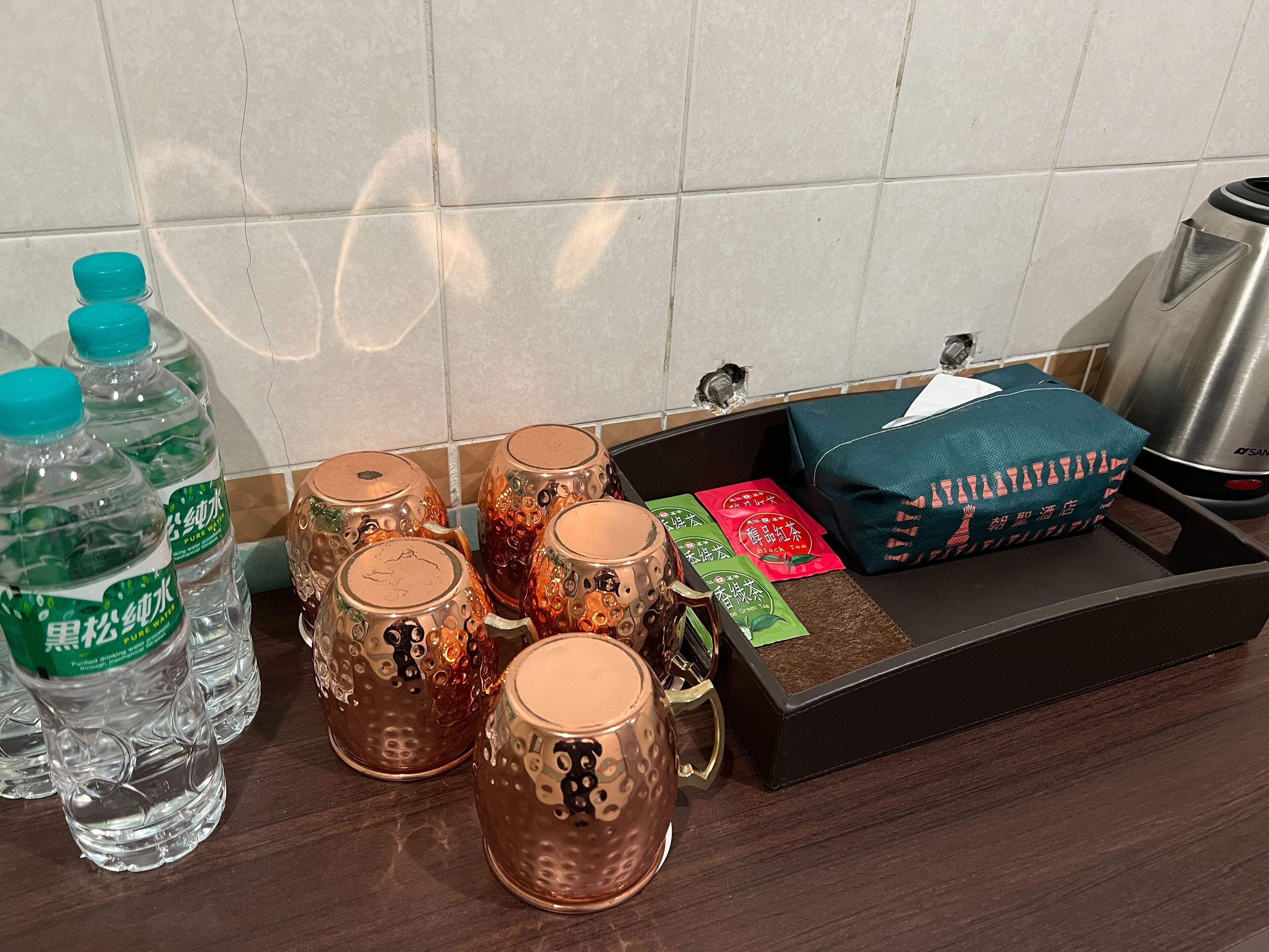 A kitchen counter with water bottles, decorative mugs, a box of tea, and a kettle.