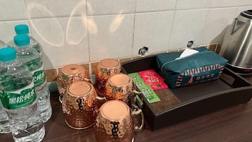 A kitchen counter with water bottles, decorative mugs, a box of tea, and a kettle.