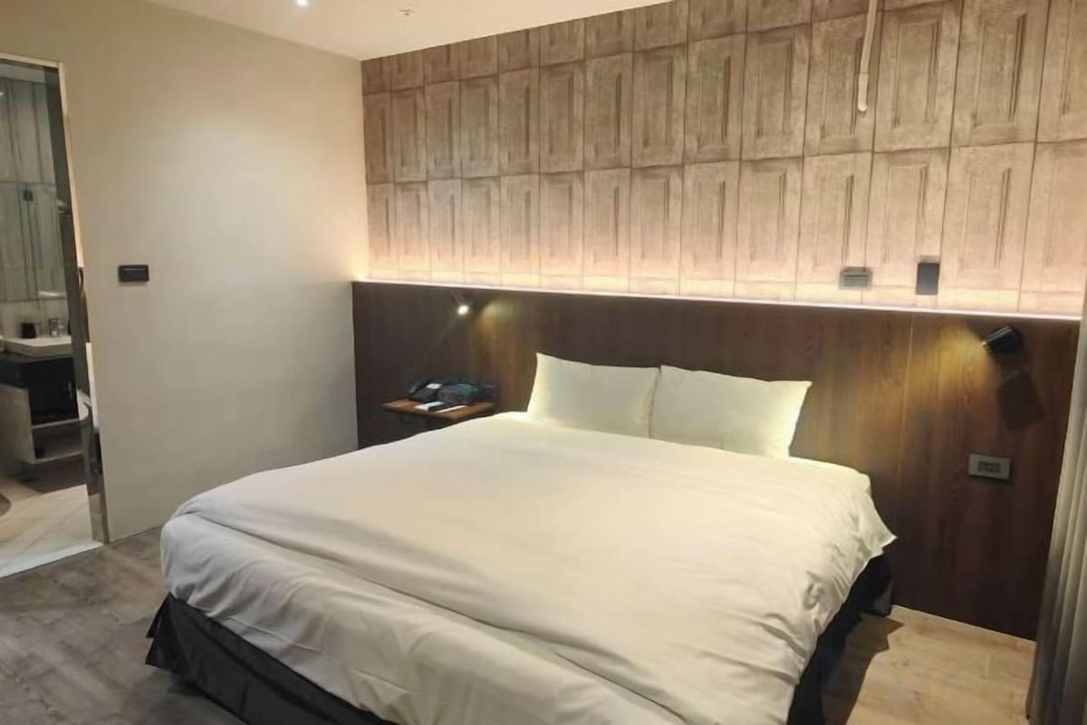 Habitación de hotel con una cama grande, cabecera de madera y mesita de noche con lámpara.