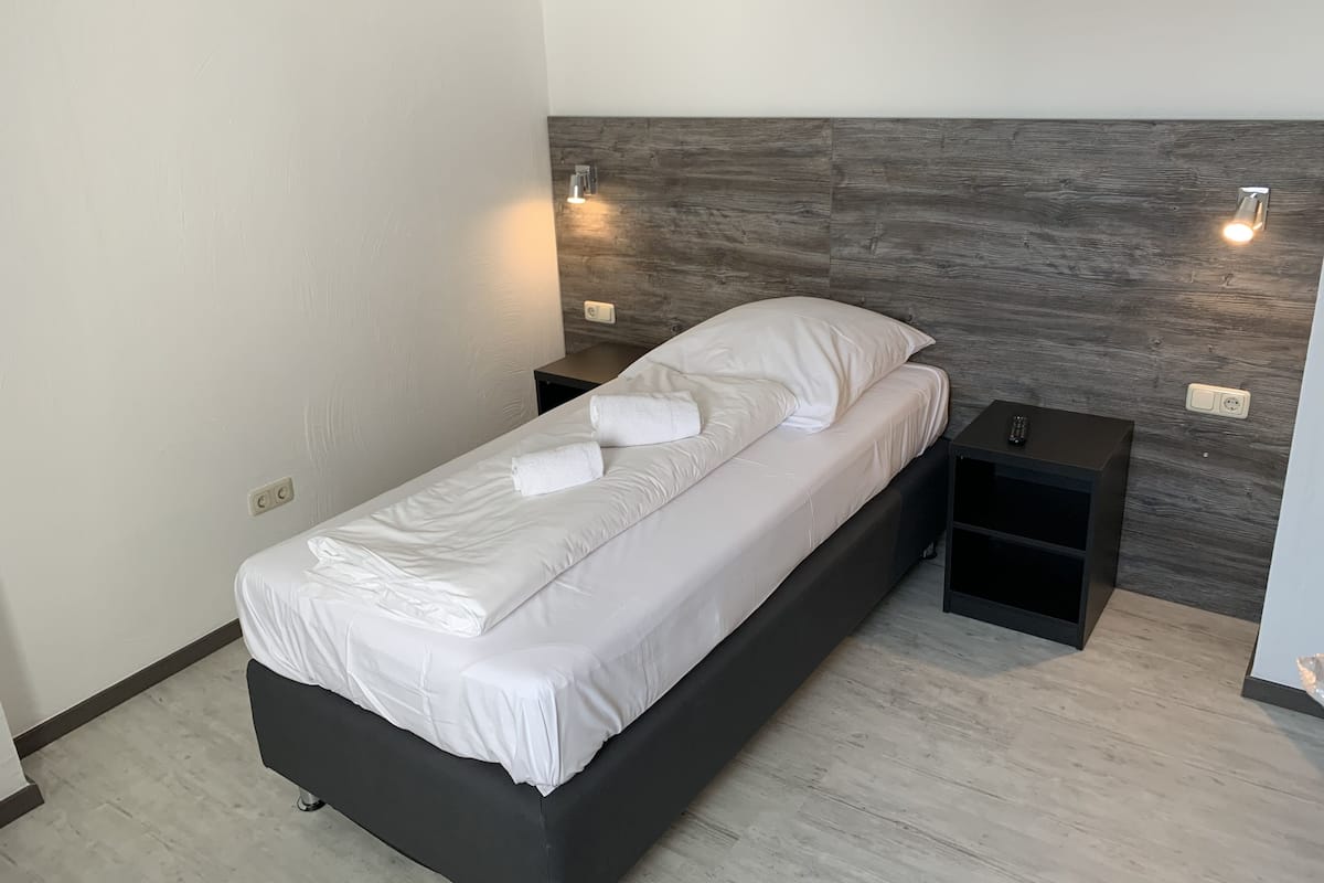 A single bed with white linens and two bedside tables, one with a remote control.
