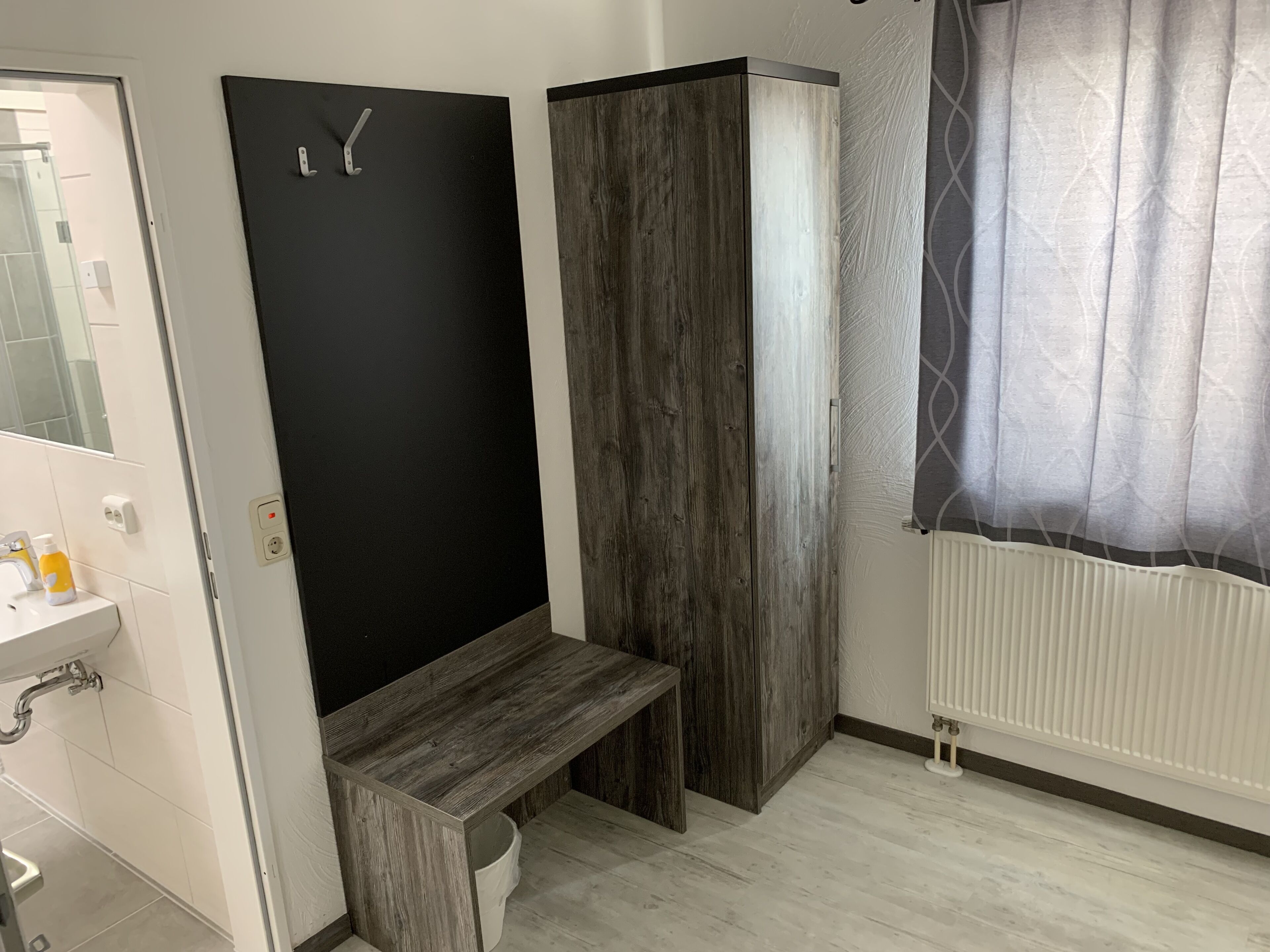A bathroom with a white sink, a black door, a wooden bench, and a radiator.