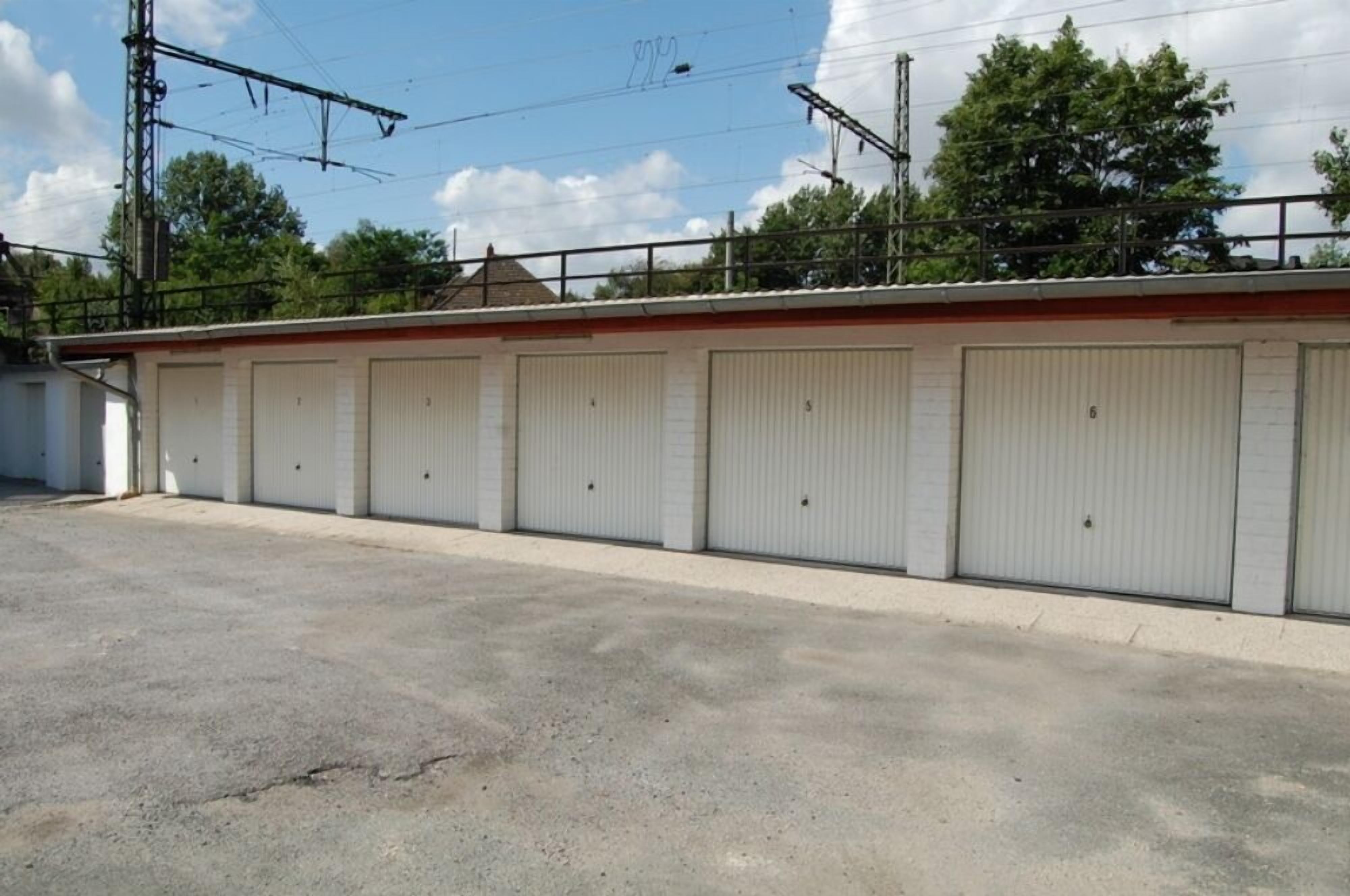 A row of closed, white metal garage doors with a flat roof and a concrete ground.