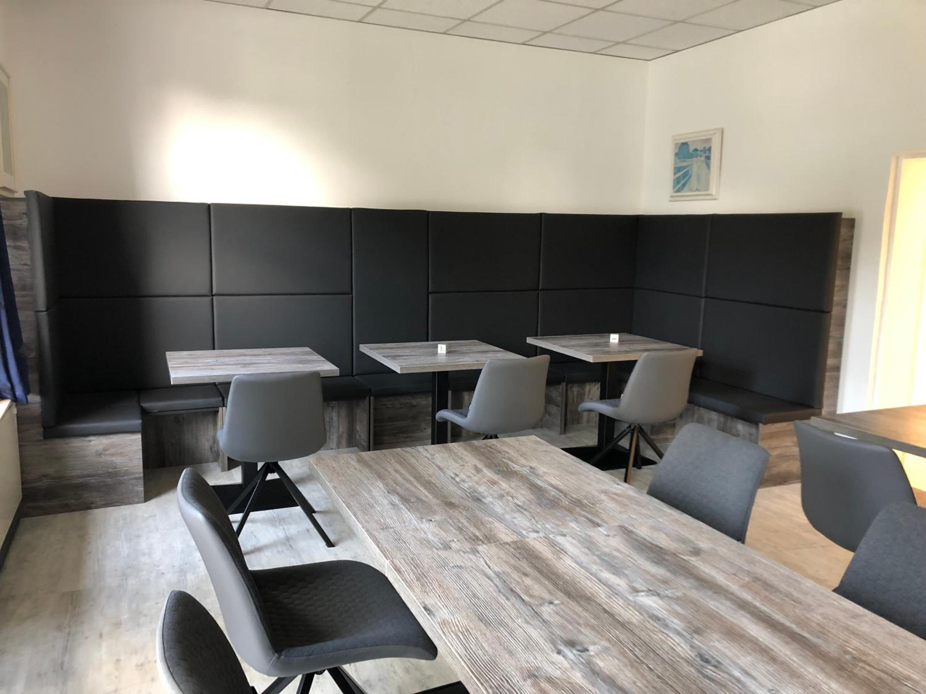 Een moderne vergaderruimte met een grote houten tafel, vier grijze stoelen en beklede, zwarte wanden.