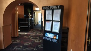 Un pasillo interior con suelo alfombrado, un mostrador de recepción y un punto de información con folletos.