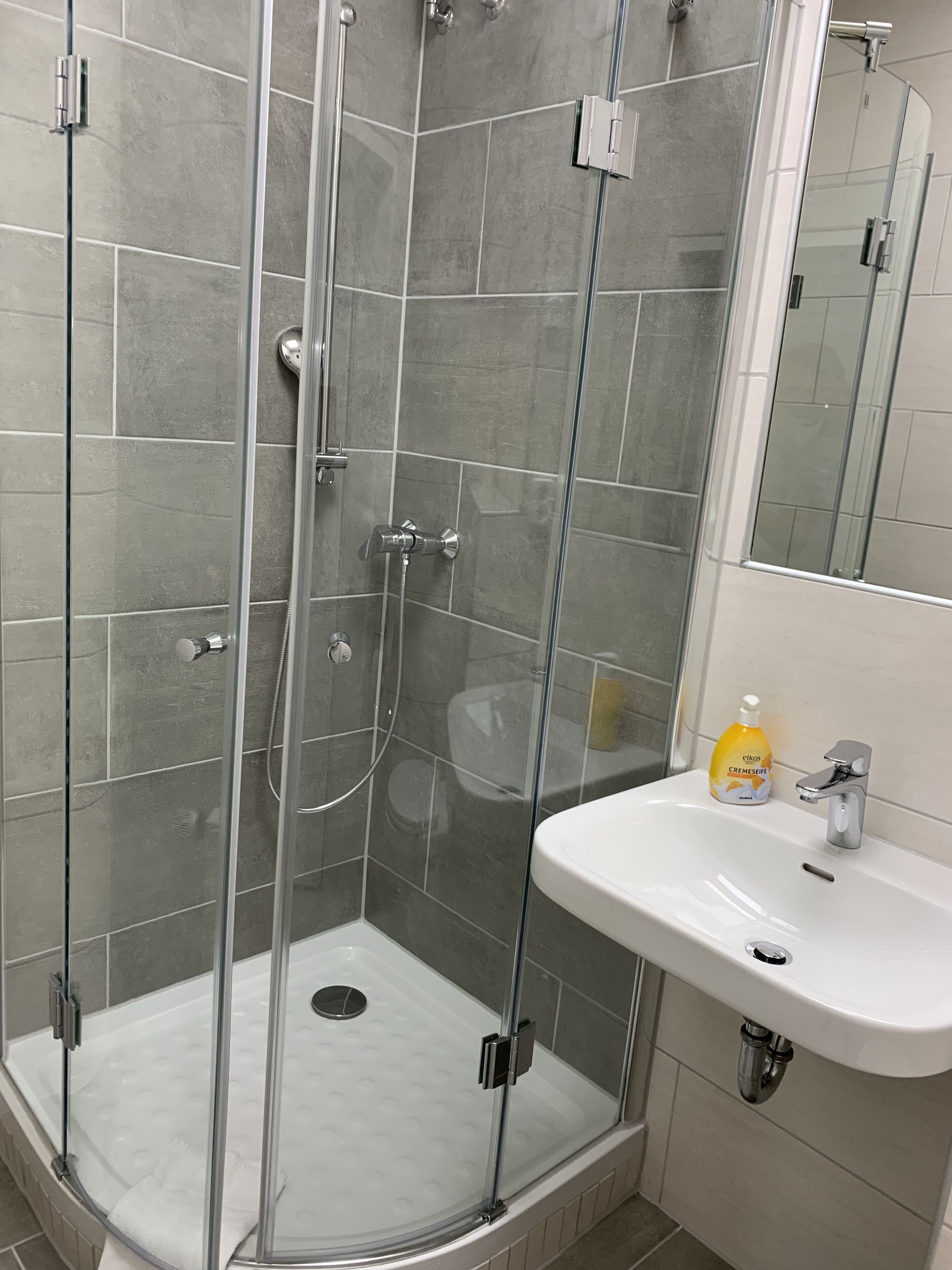 A modern bathroom with a glass-enclosed shower, a white sink, and a mirror above it.