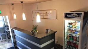 Un área de recepción con mostrador, un cartel que dice "Recepción" y una máquina expendedora etiquetada "Cool & Trendy".