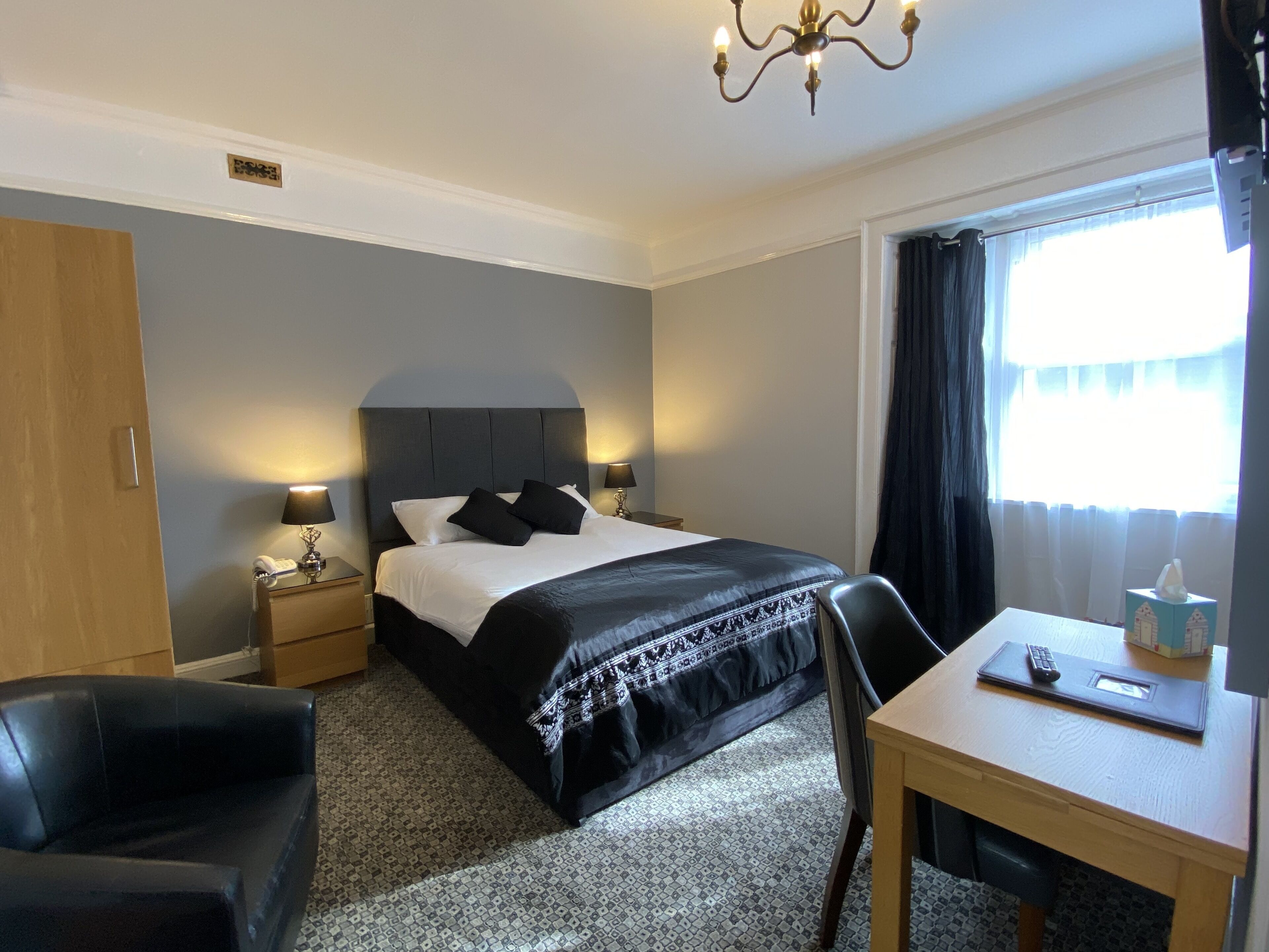 A hotel room with a bed, bedside lamps, a desk, a chair, and a window with curtains.