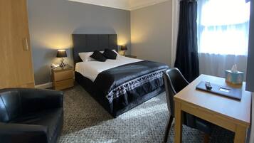 A hotel room with a bed, bedside lamps, a desk, a chair, and a window with curtains.