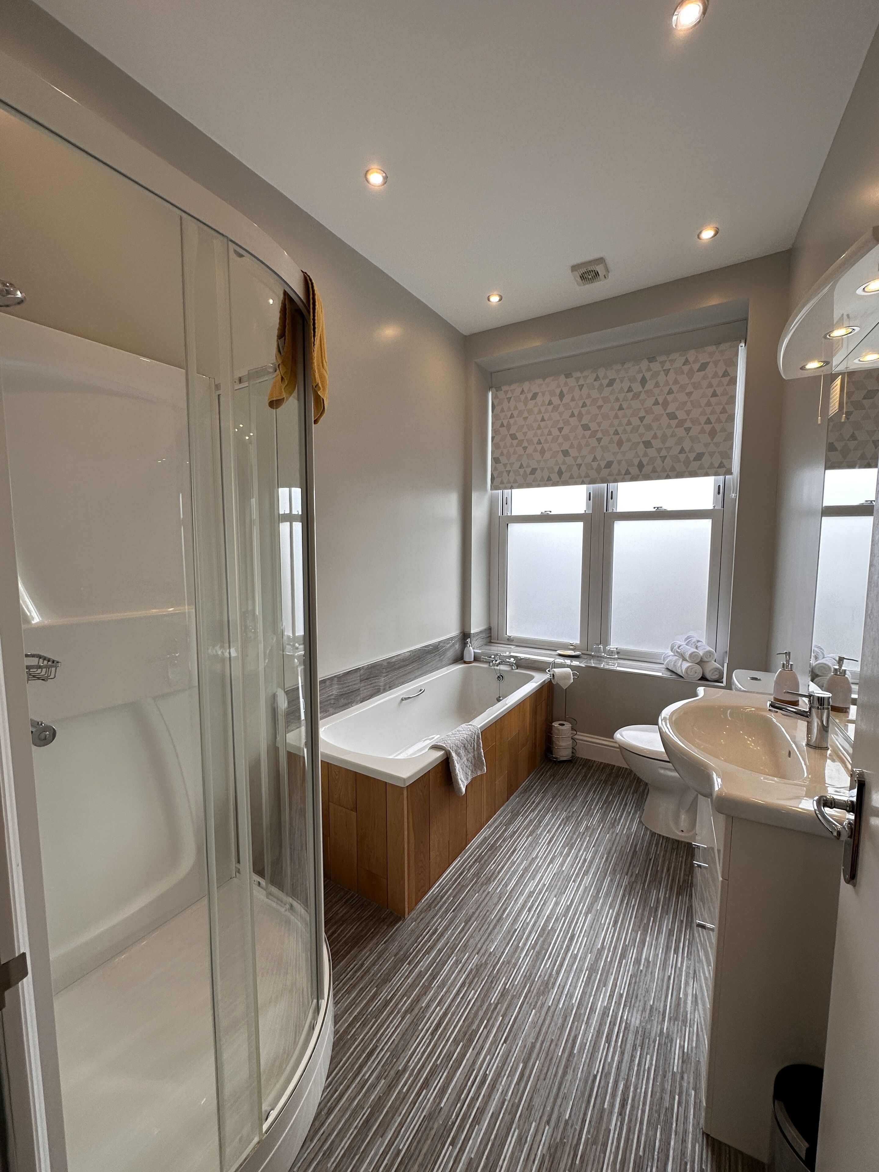 A modern bathroom with a glass shower enclosure, a freestanding bathtub, a vanity with a sink, and a toilet.