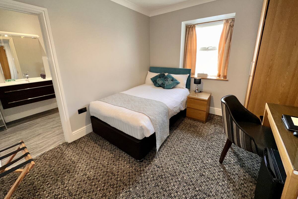 A bedroom with a bed, bedside table, lamp, chair, and a window with curtains.