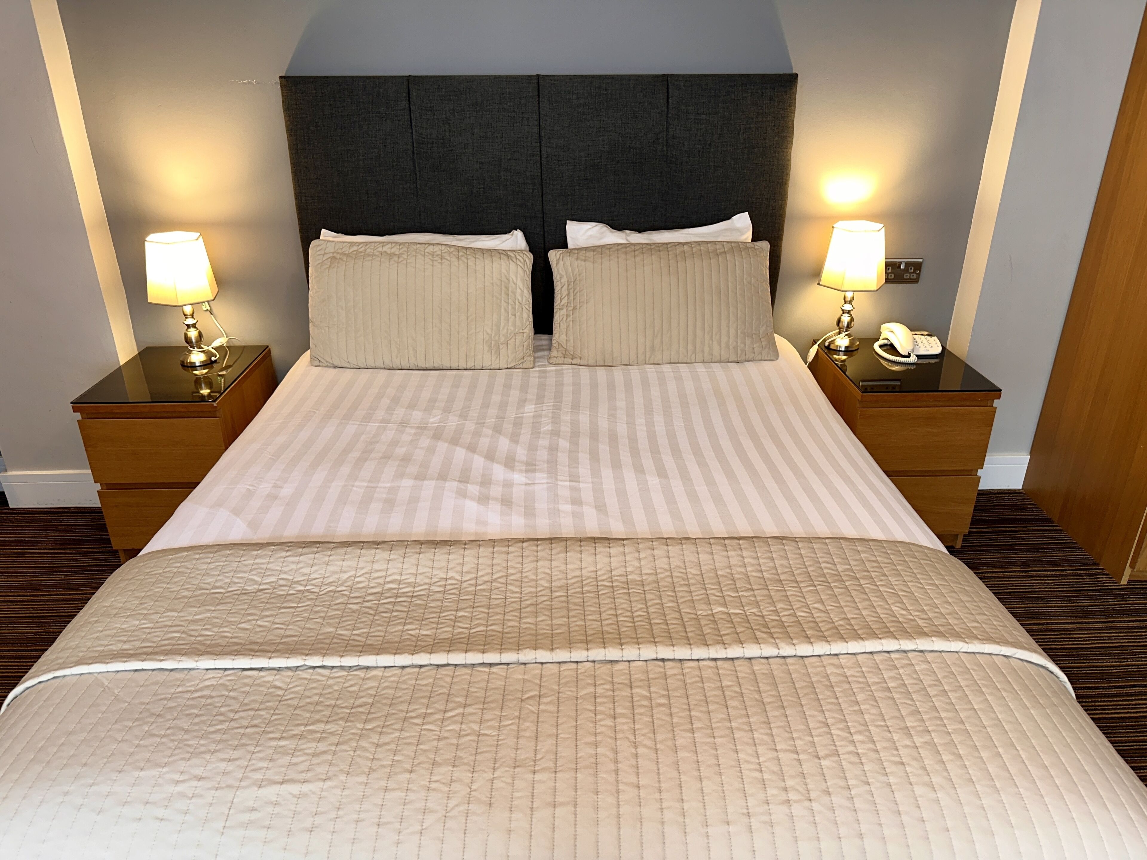 A neatly made bed with striped bedding and two pillows, flanked by nightstands with lamps and a phone.