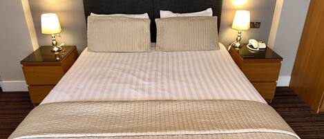 A neatly made bed with striped bedding and two pillows, flanked by nightstands with lamps and a phone.