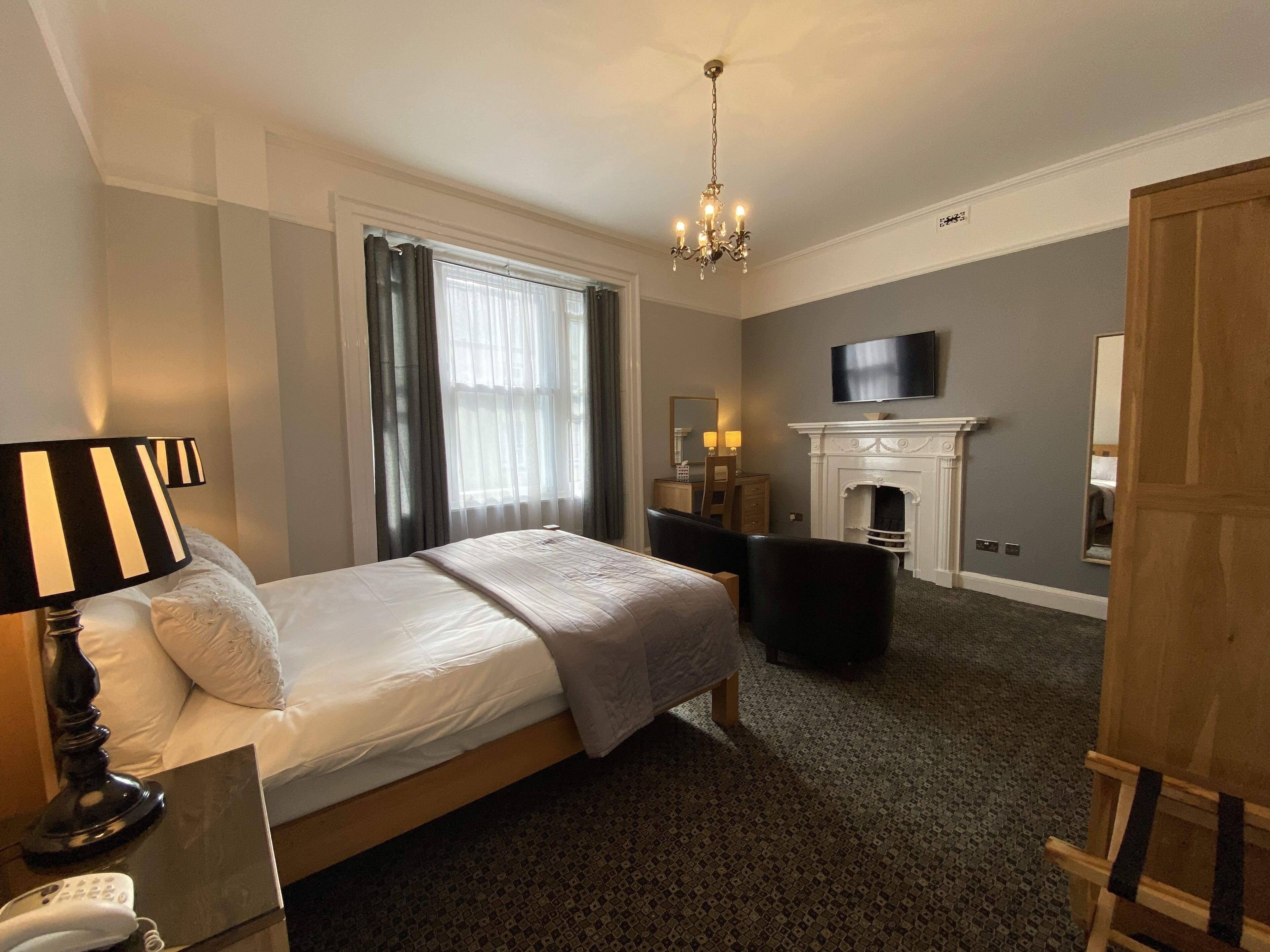 Ein Hotelzimmer mit Bett, Schreibtisch, Stuhl, Fernseher, Kamin und einer Chandelier.