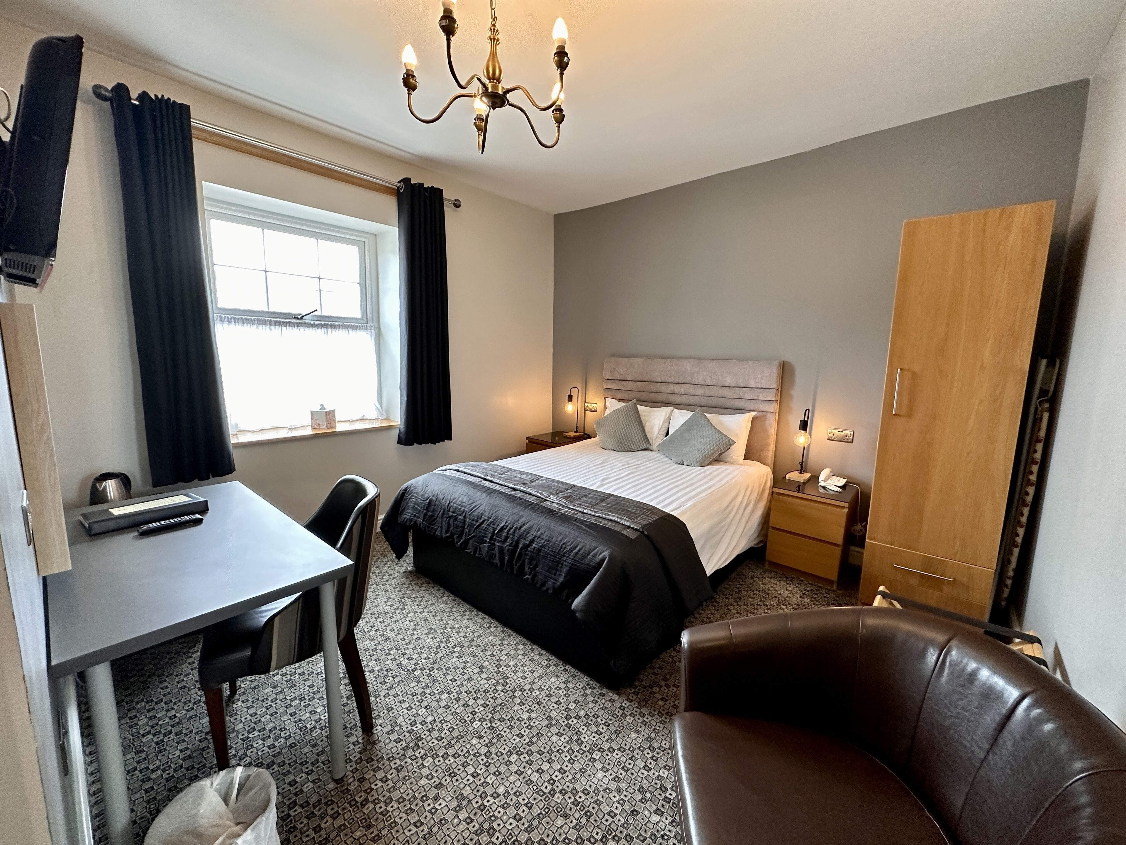 Una habitación de hotel con cama, escritorio, silla, armario y ventana con cortinas.