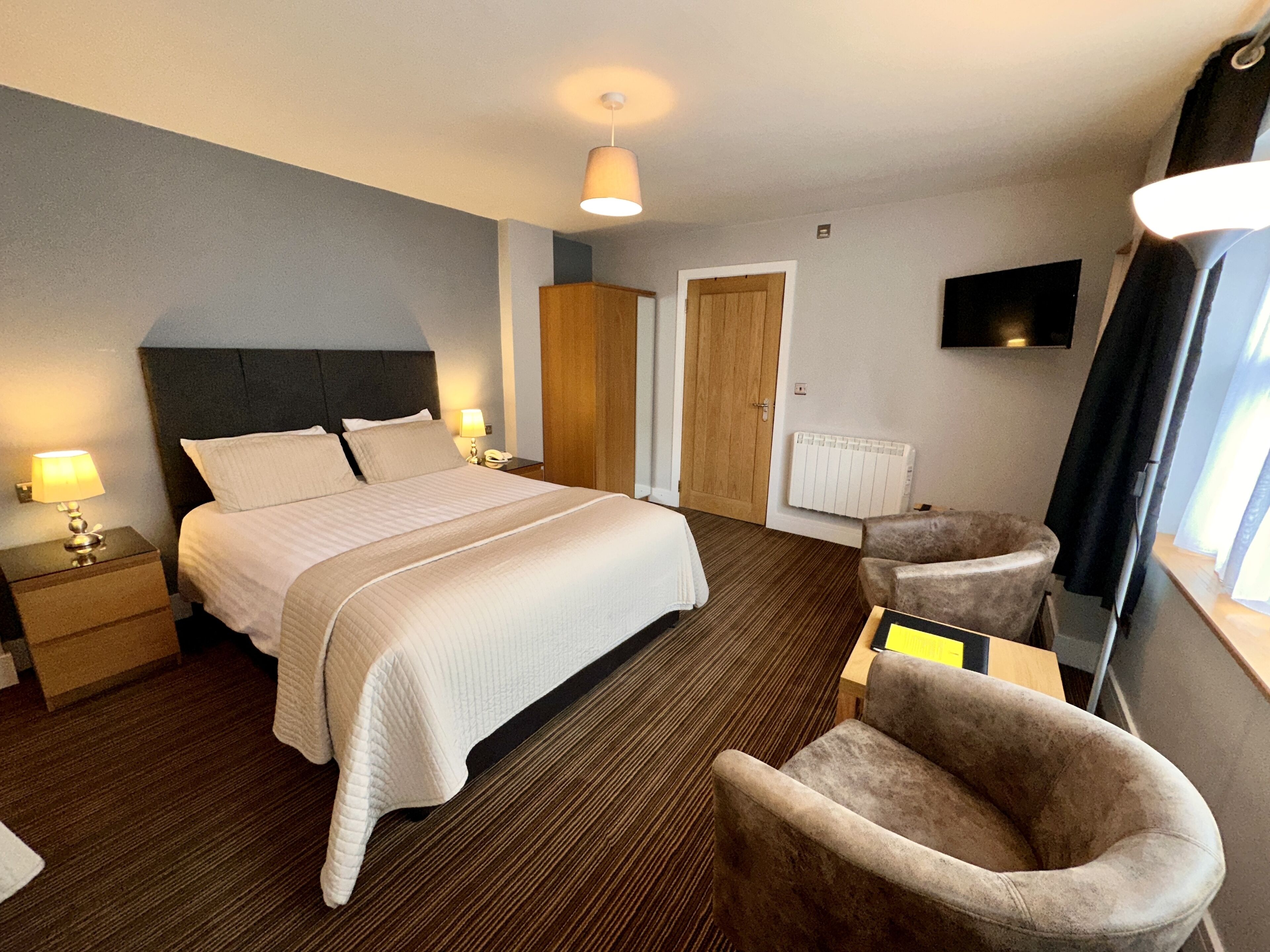A hotel room with a large bed, bedside tables with lamps, a chair, a television, and a door.