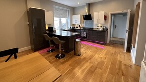 A modern kitchen with a central island, bar stools, a dining table, and a refrigerator.