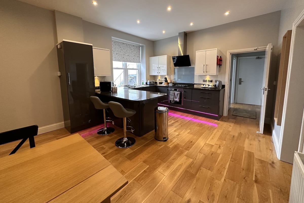 A modern kitchen with a central island, bar stools, a dining table, and a refrigerator.