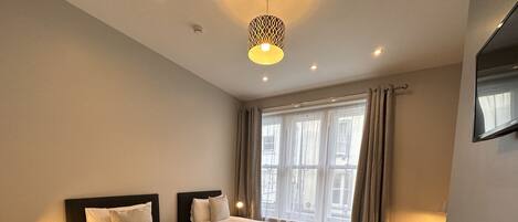 Habitación de hotel con dos camas, un escritorio y una ventana con cortinas.