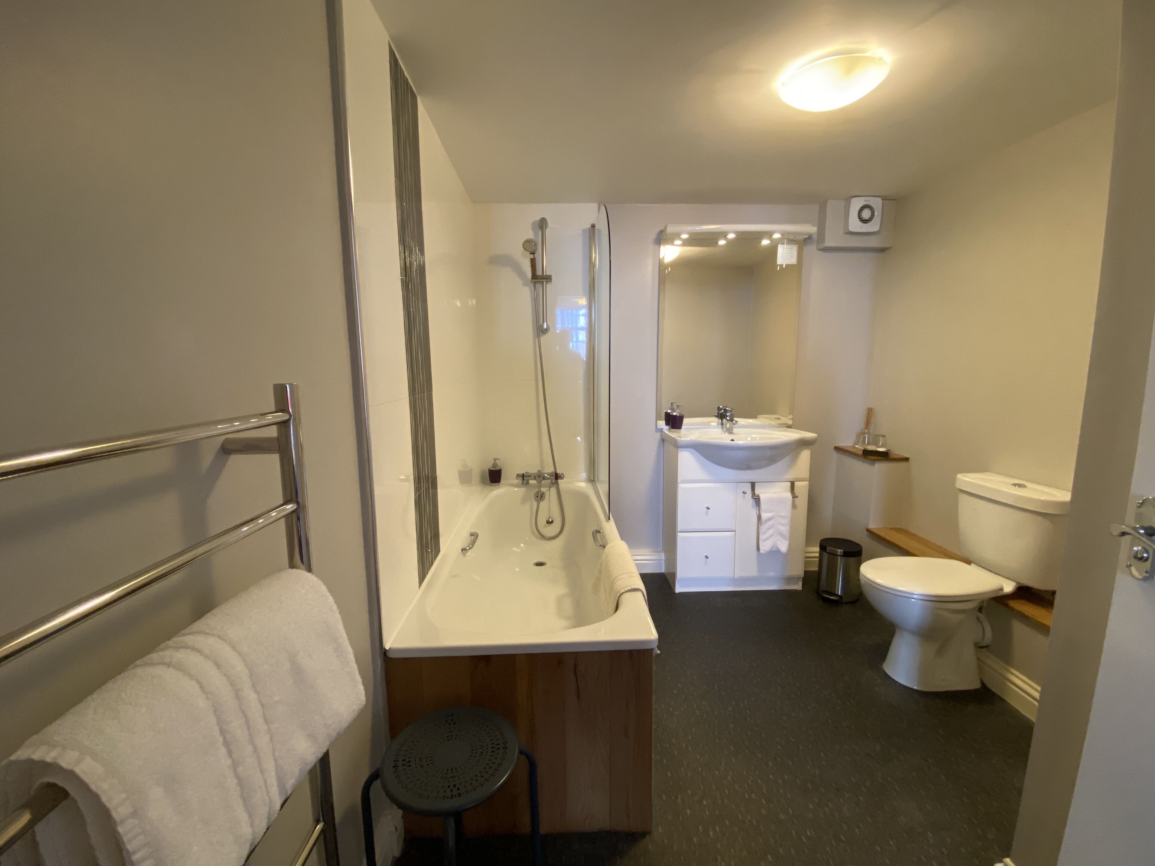 Un baño moderno con ducha, lavabo, inodoro y un taburete pequeño.