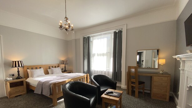 A hotel room with a bed, a desk, a chair, a lamp, and a mirror.