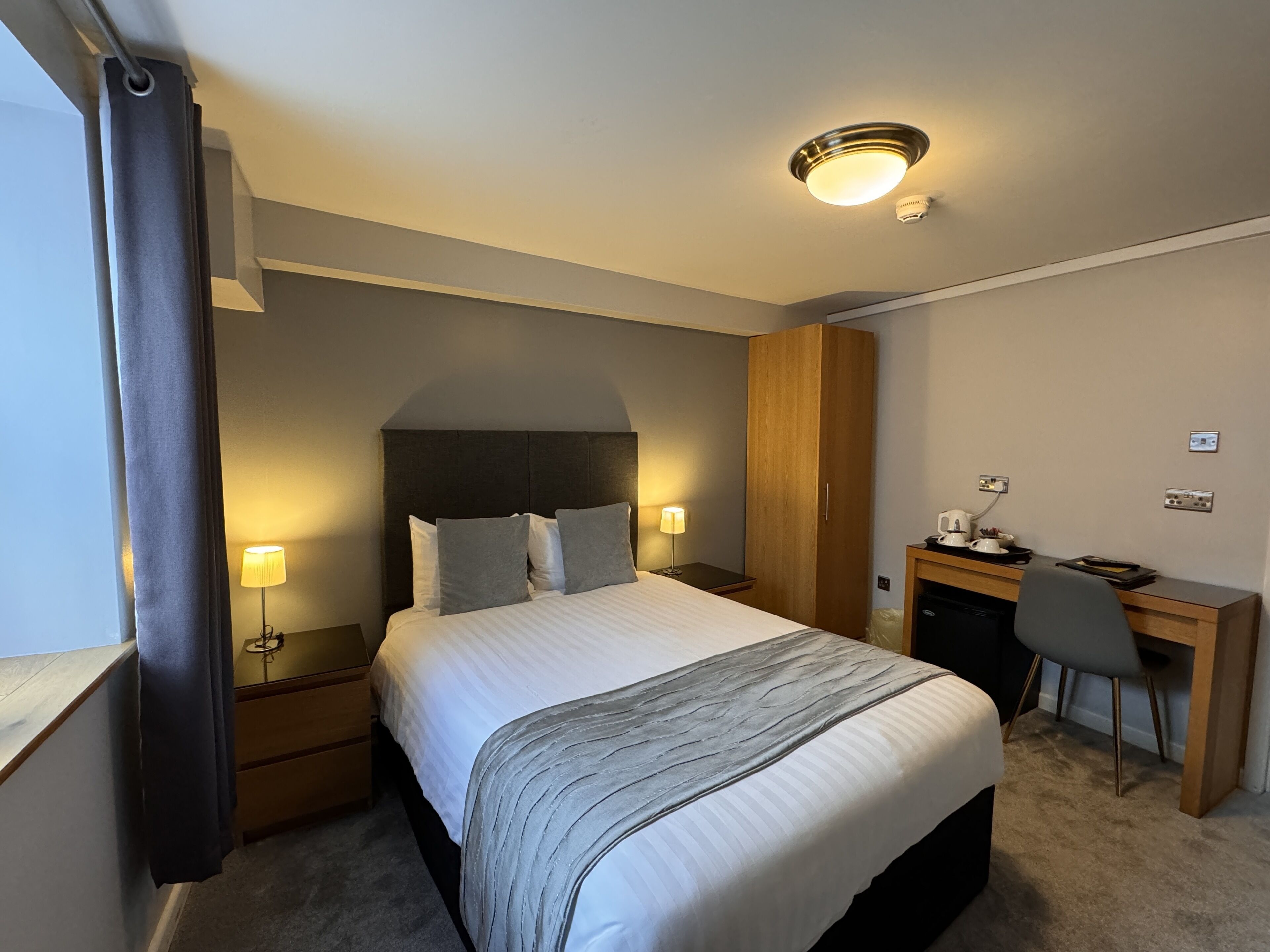 A hotel room with a bed, bedside lamps, a desk, and a chair.