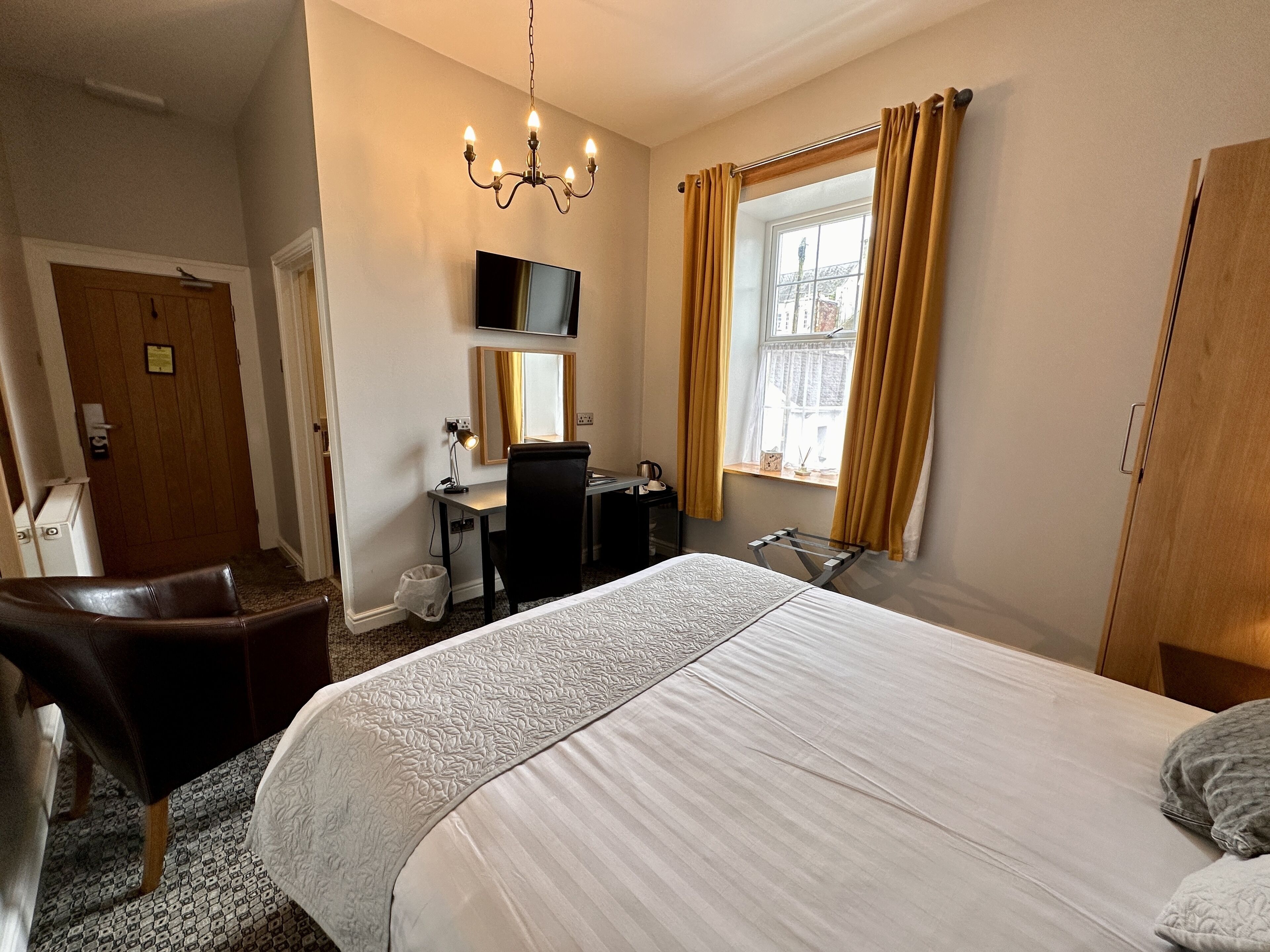 Habitación de hotel con cama, escritorio, silla, televisor y ventana con cortinas.