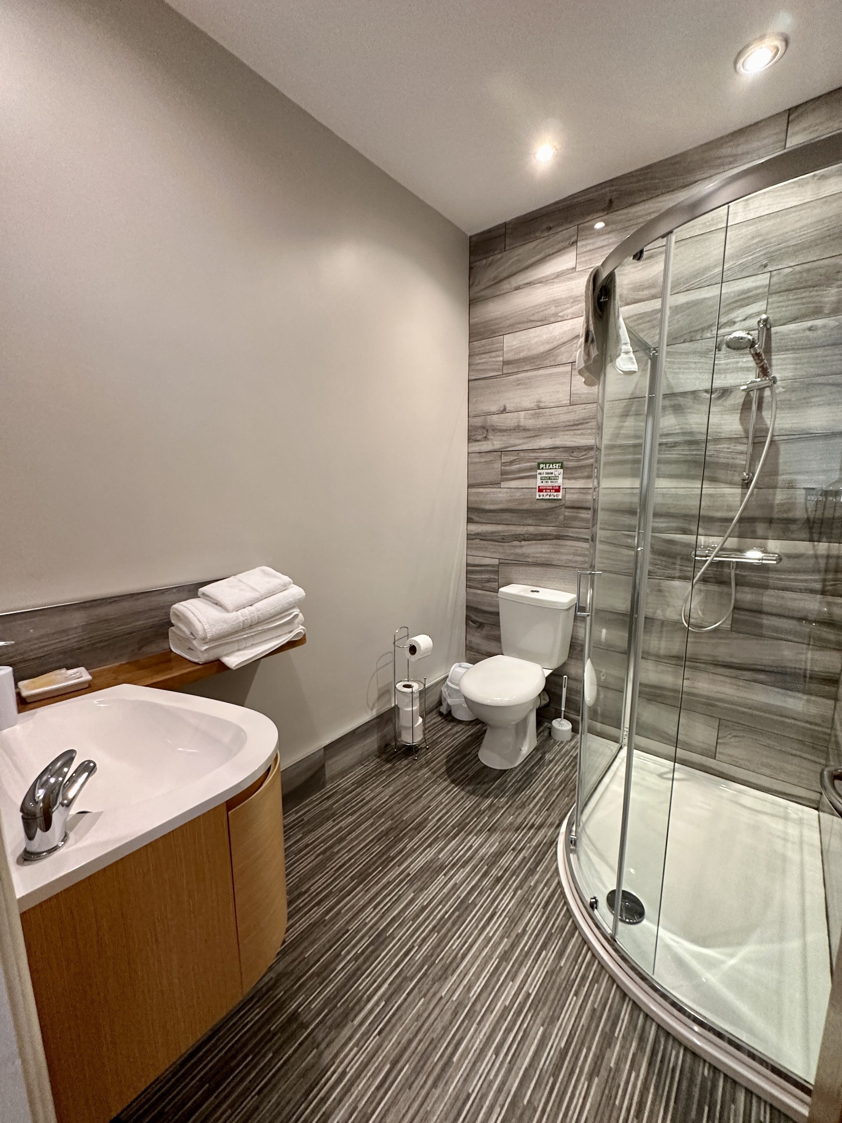 A modern bathroom with a glass shower enclosure, a sink with a wooden vanity, and a toilet.