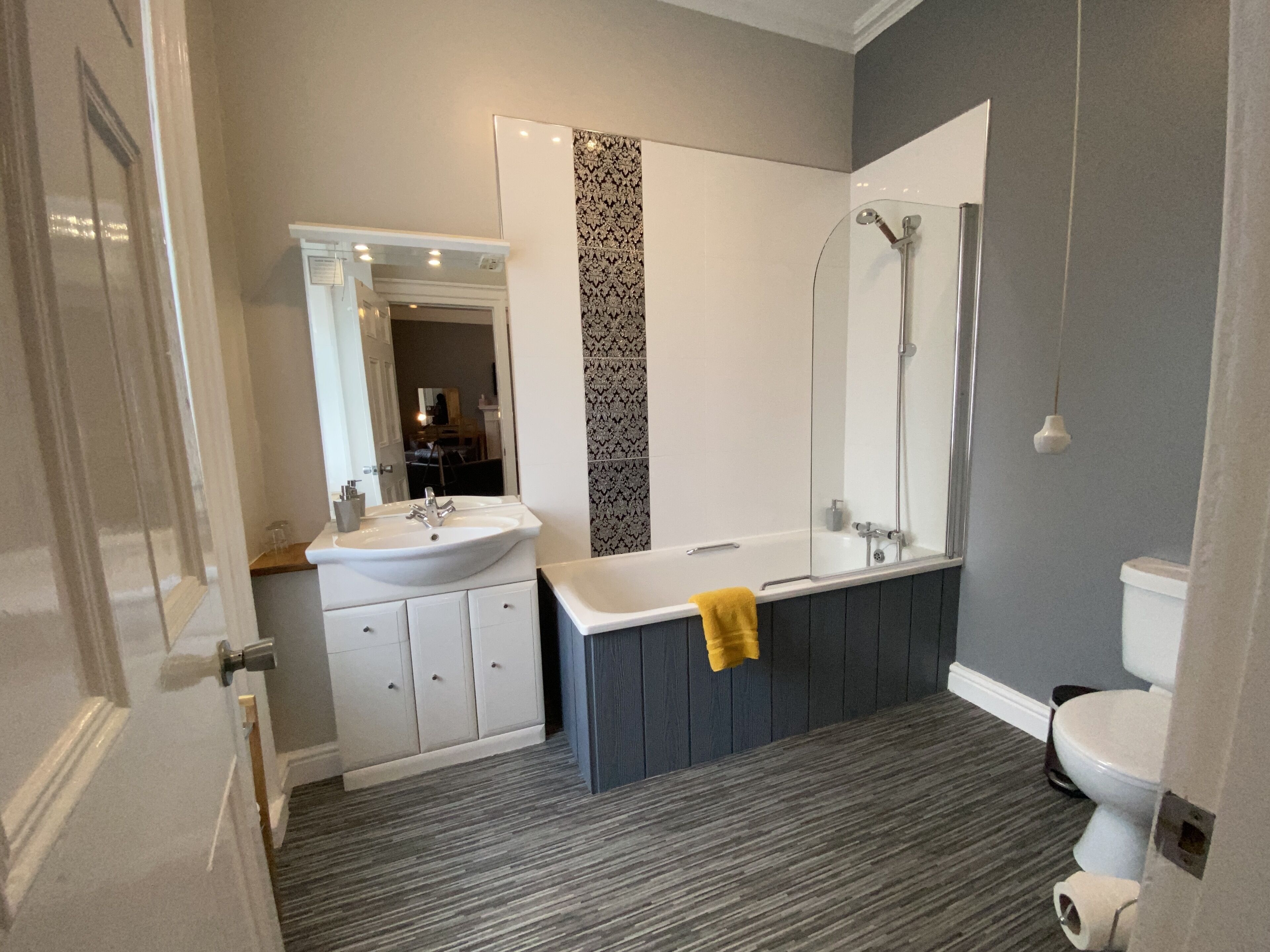 Un baño moderno con un lavamanos blanco, tocador de madera oscura, una bañera con una toalla amarilla y una ducha.