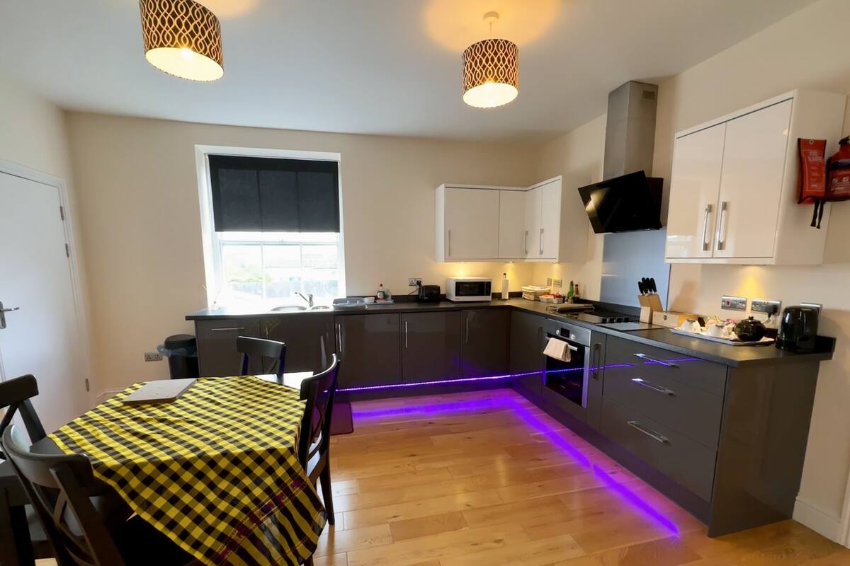 A modern kitchen with a central island, wooden flooring, and pendant lighting.