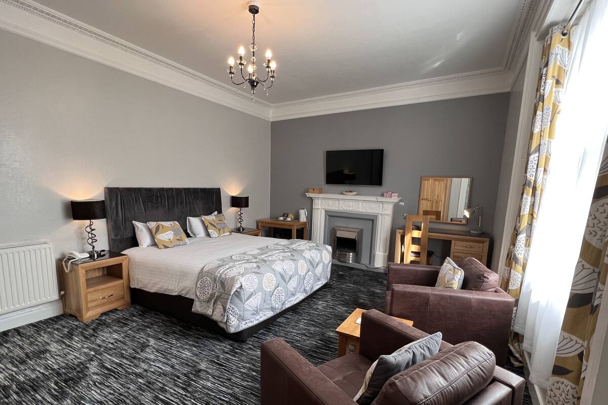 A hotel room with a large bed, a fireplace, a television, and a seating area with a sofa and armchair.