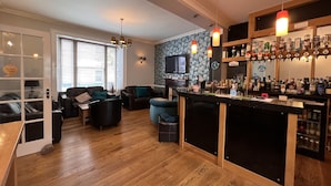 A modern living room with a bar area, wooden flooring, and a television mounted on the wall.