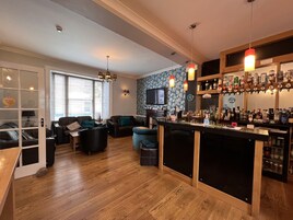 Una sala de estar moderna con una zona de bar, piso de madera y un televisor montado en la pared.