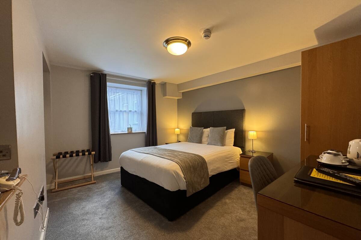 A hotel room with a bed, bedside lamps, a desk with a telephone, and a radiator.