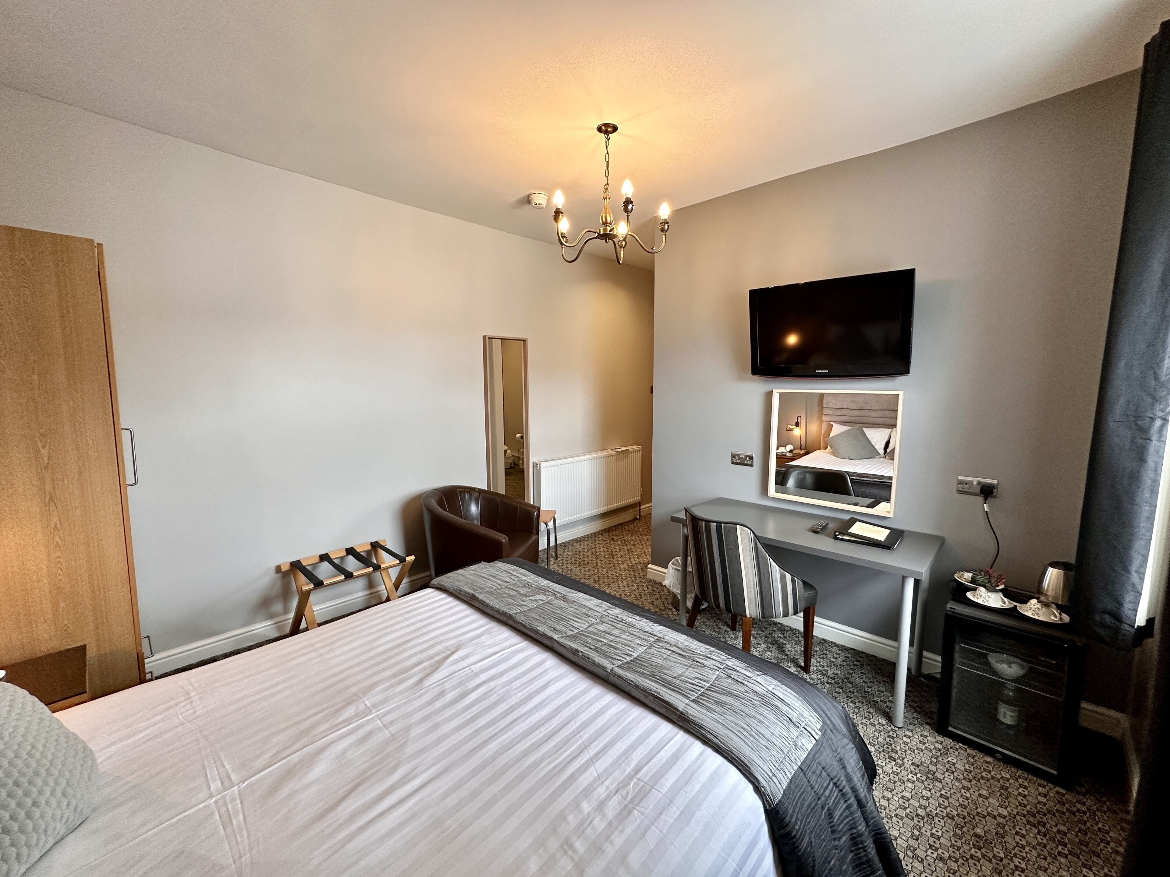 Habitación de hotel con una cama grande, un escritorio, una silla, un televisor y un espejo.