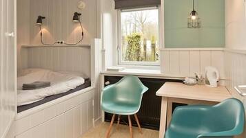 Une chambre à coucher de taille réduite, avec un lit superposé, une fenêtre offrant une vue agréable, un bureau avec des chaises et des lampes fixées au mur.