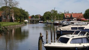 Un canal bordé de bateaux amarrés sur la droite, un pont en arrière-plan et des maisons sur la gauche.