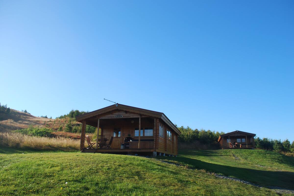 A wooden cabin with a porch, a covered outdoor seating area, and a small deck.