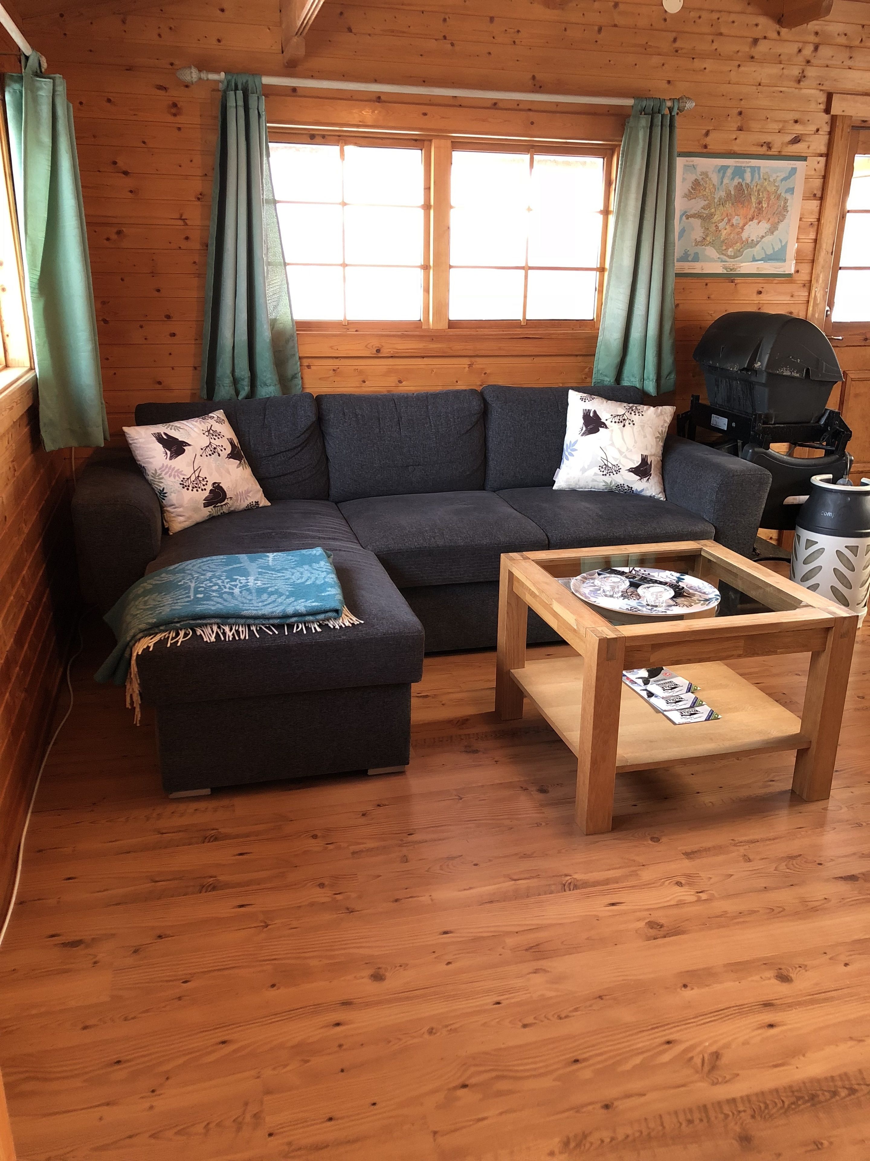 Un interior de cabaña acogedor con un sofá gris oscuro, una mesa de centro de madera y un pequeño reposapiés.