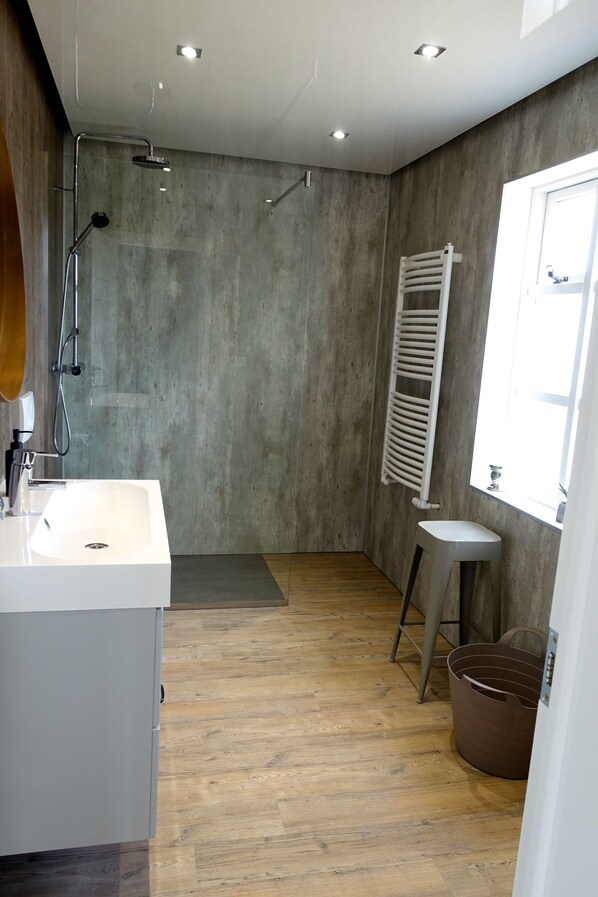 A modern bathroom with a large shower, a sink, and a window providing natural light.