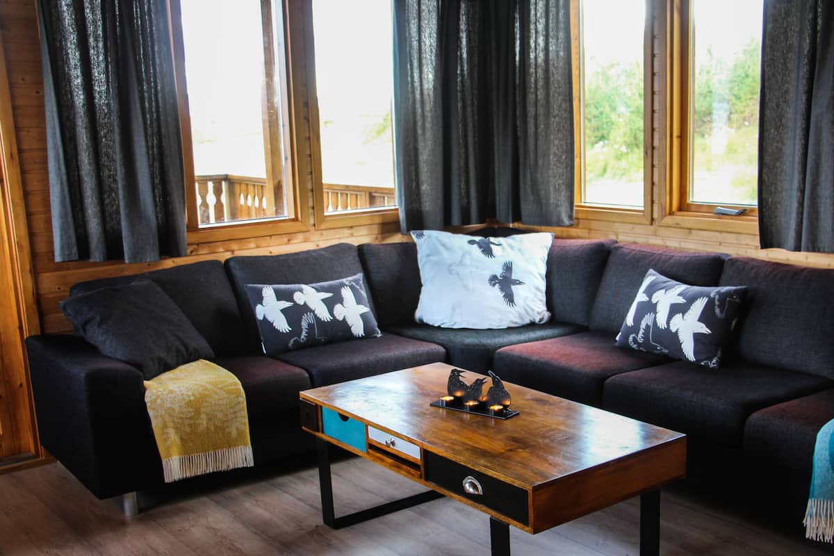 A cozy living room with a sectional sofa, a wooden coffee table, and large windows with curtains.