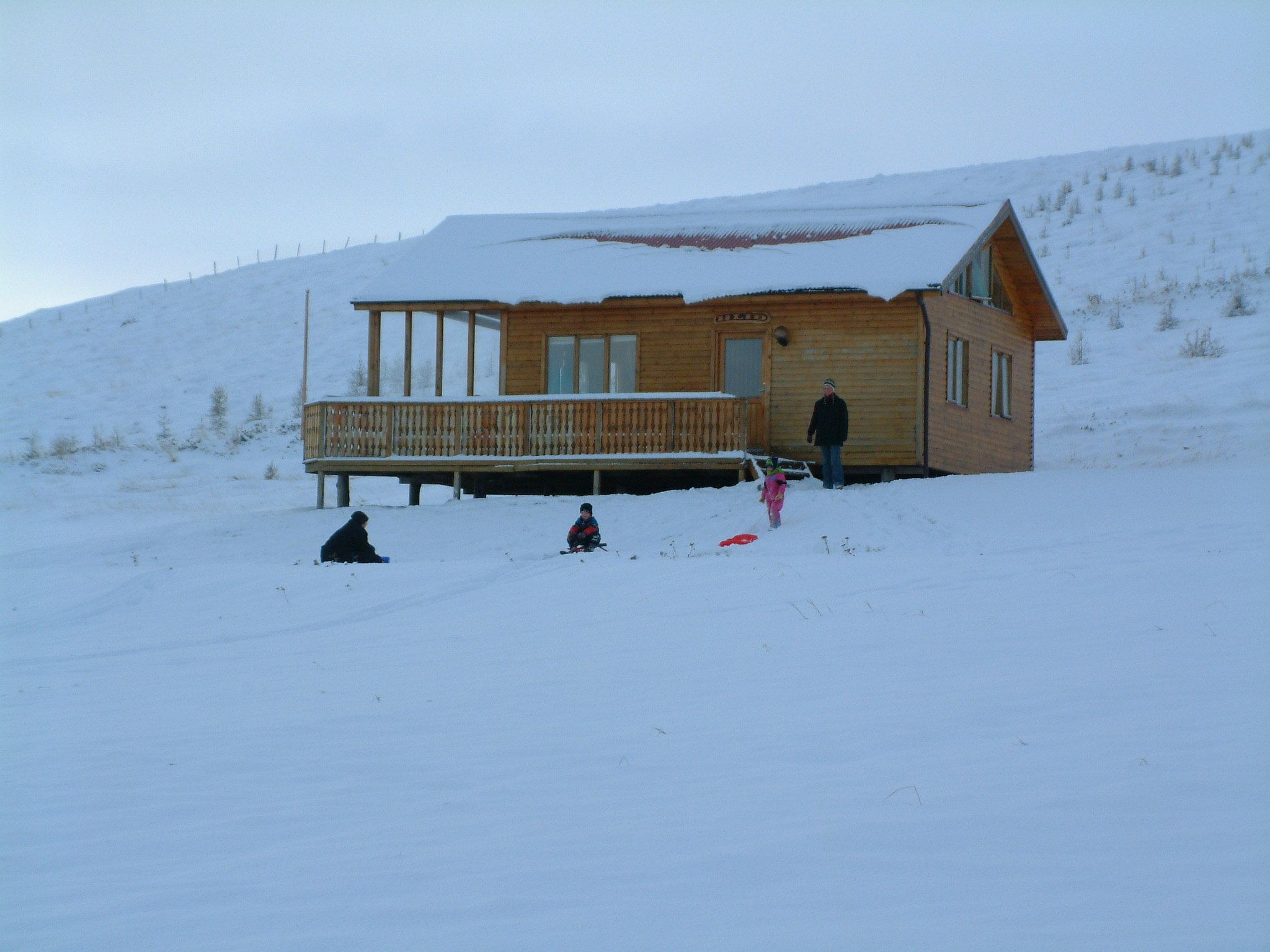A wooden cabin with a balcony, surrounded by snow-covered ground.