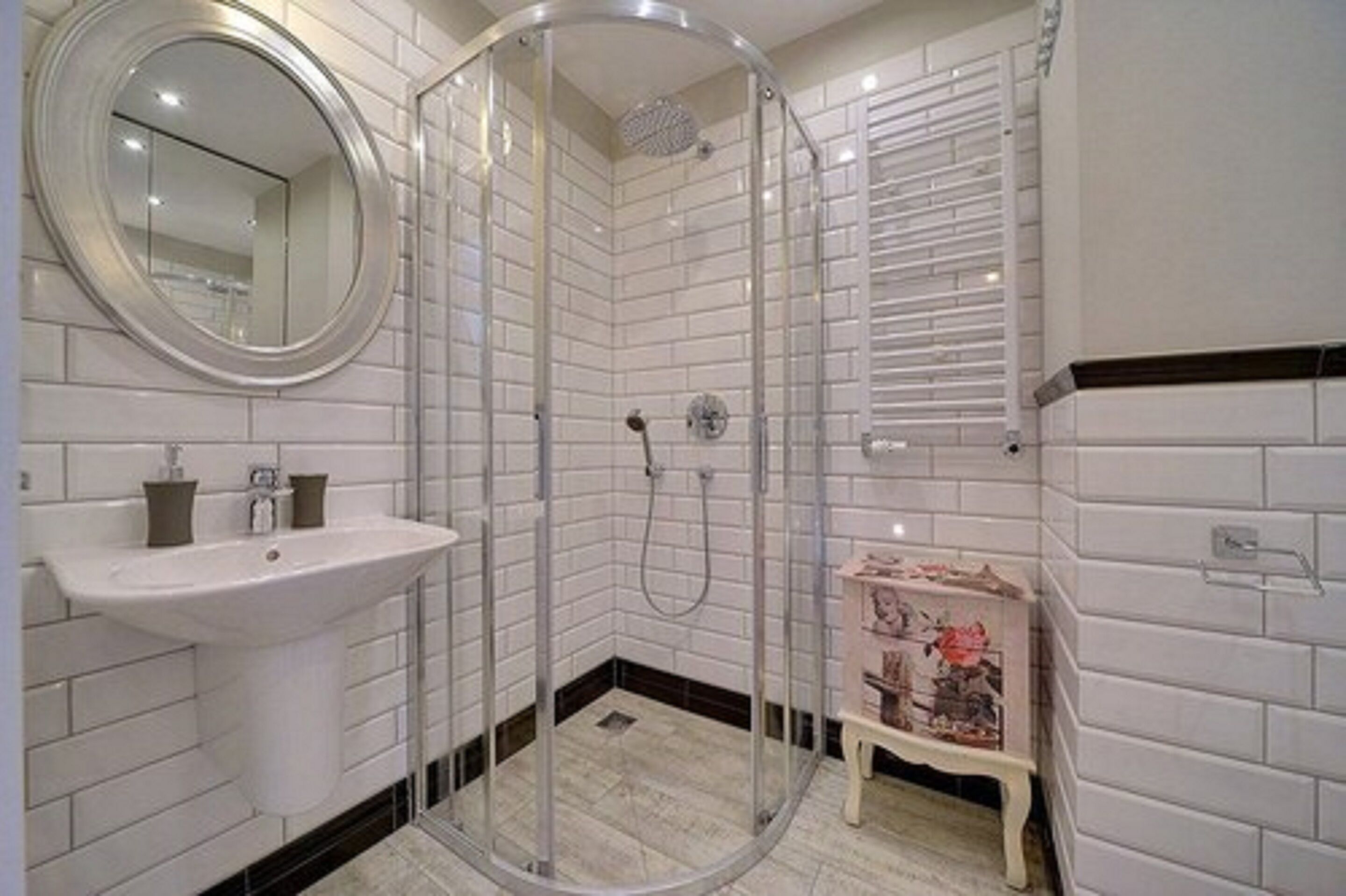 Uma casa de banho moderna com chuveiro em cabine de vidro, lavatório branco e uma pequena prateleira decorativa.