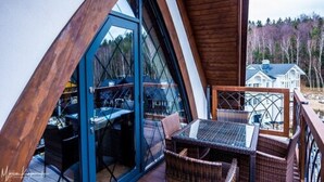 Une pièce triangulaire dotée d'une grande fenêtre, de meubles en osier et offrant une vue sur une maison au loin.