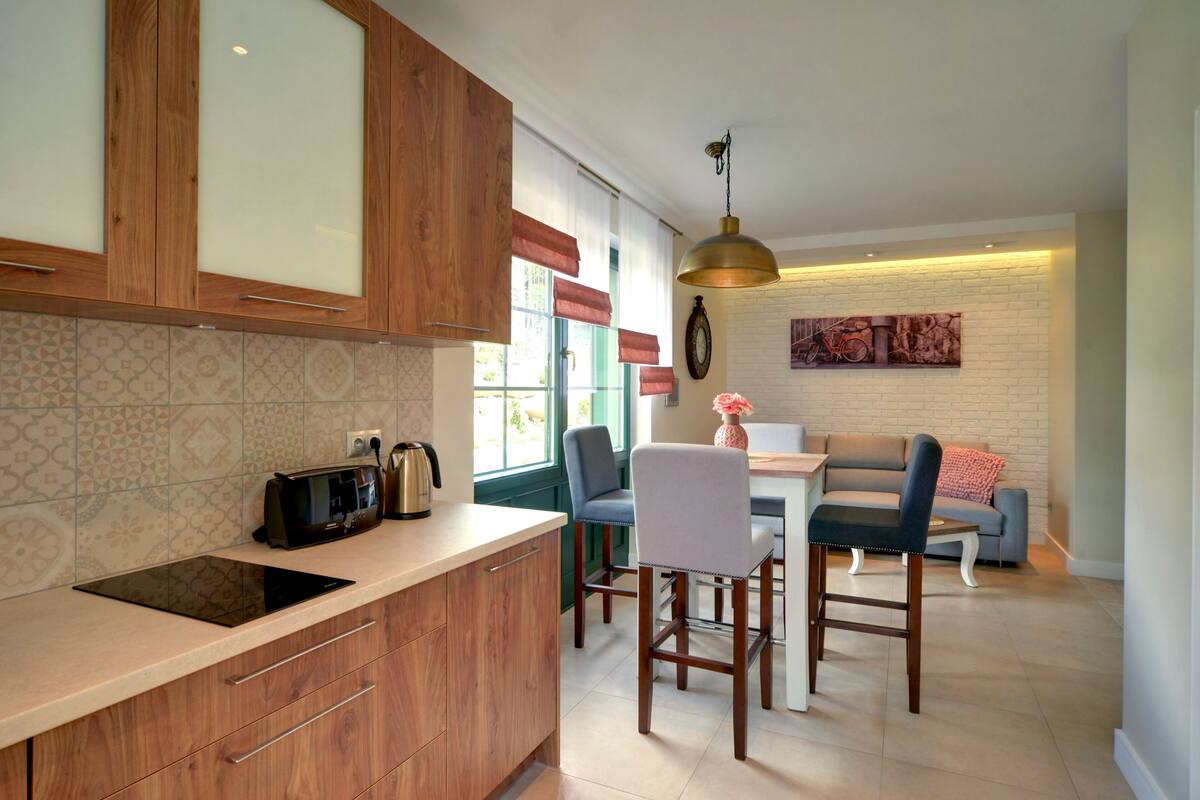 A modern kitchen with wooden cabinets, a built-in oven, and a dining area with a table and chairs.