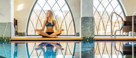 A person meditating by a pool with arched windows.
